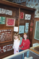 Two women standing in a room with many different types of eye glasses on the wall.